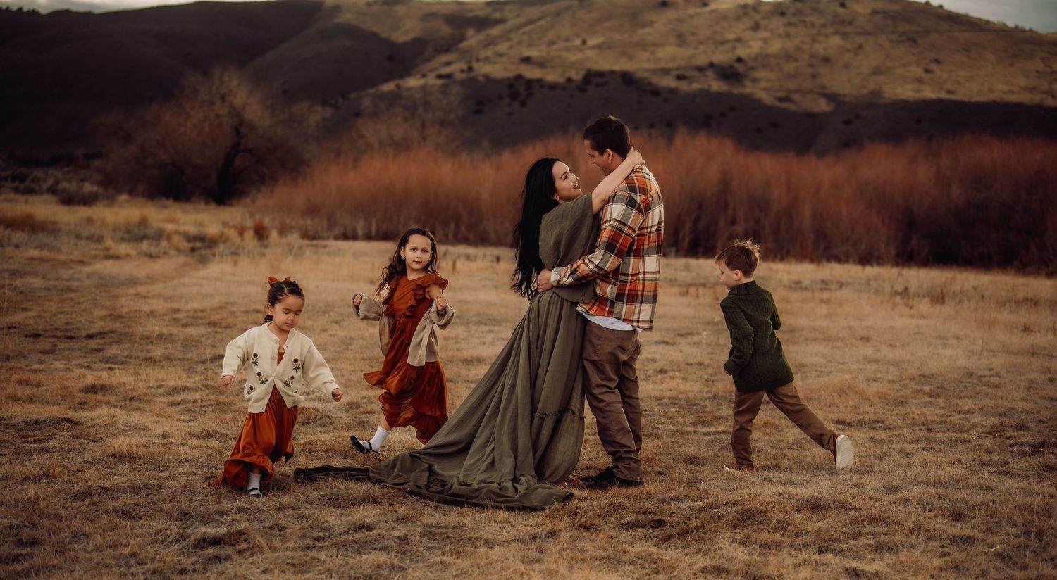A group in vintage-style clothing runs joyfully through a golden autumn field against a mountainous backdrop.