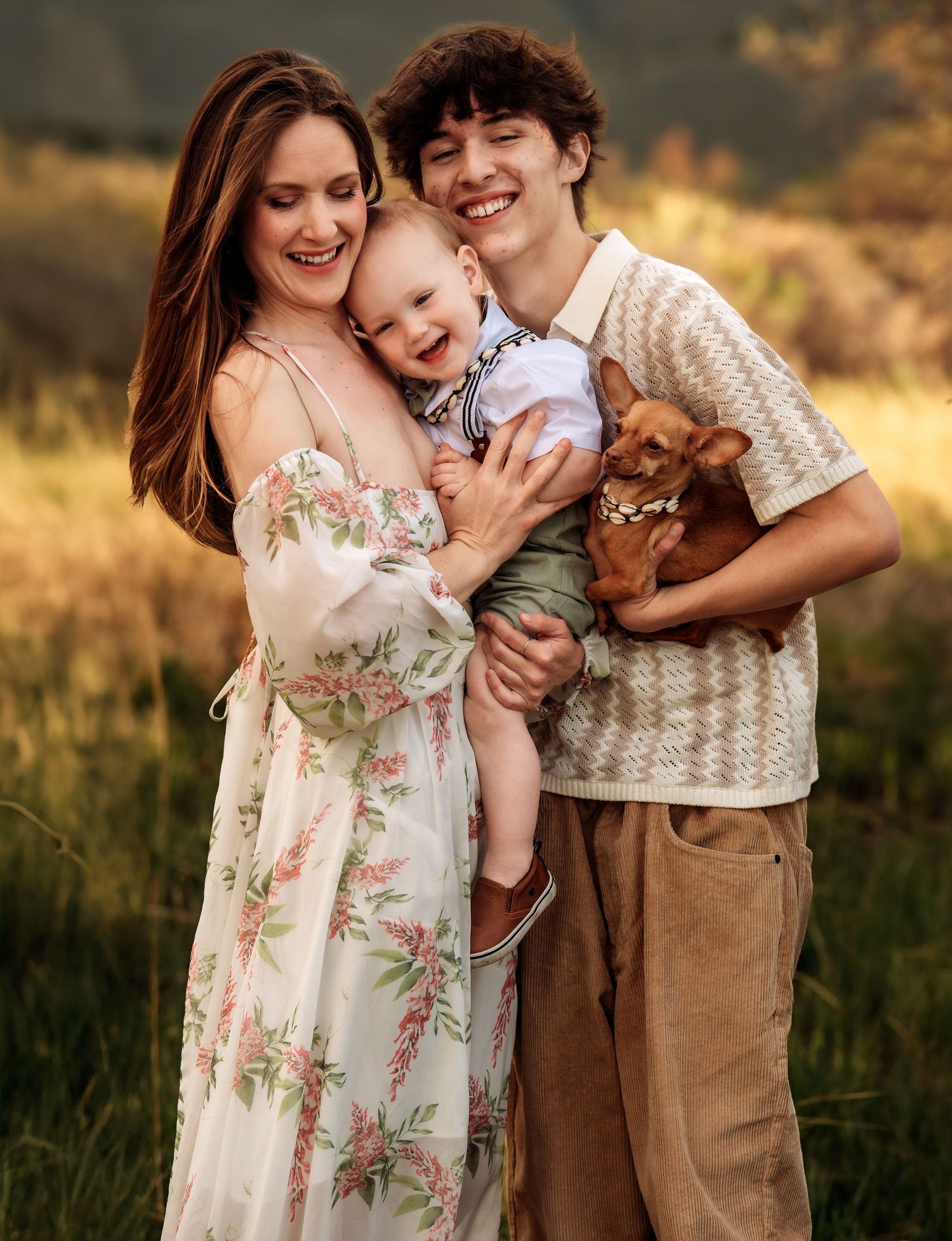 A family shares tender moments together in a sunlit field during golden hour while wearing vintage-inspired clothing.