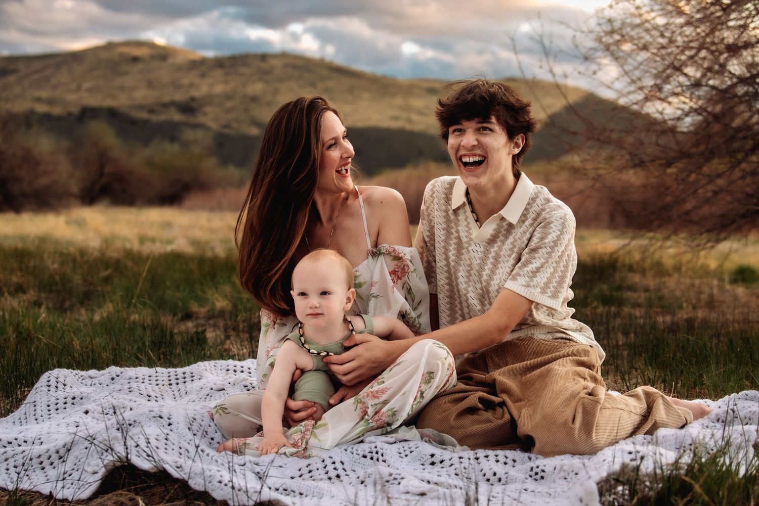 A couple shares intimate moments on a white blanket in a scenic mountain landscape during golden hour.