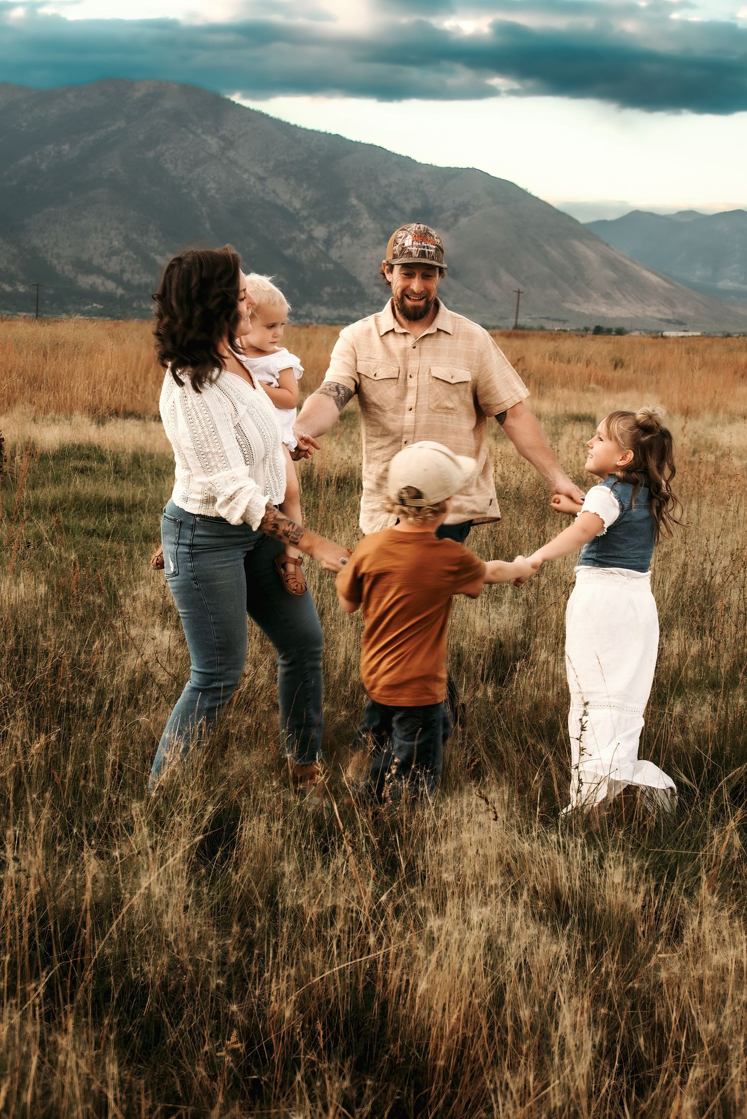 A family dances together in a golden field with mountains in the background during sunset.