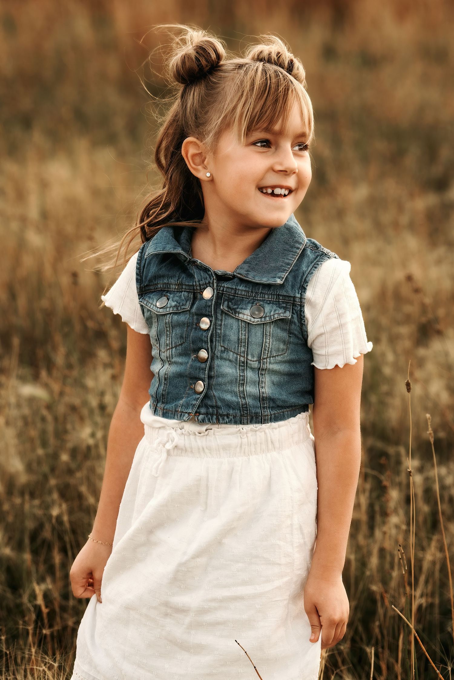 A series of four photos showing a child in a denim vest and white dress playing in a golden field at sunset.