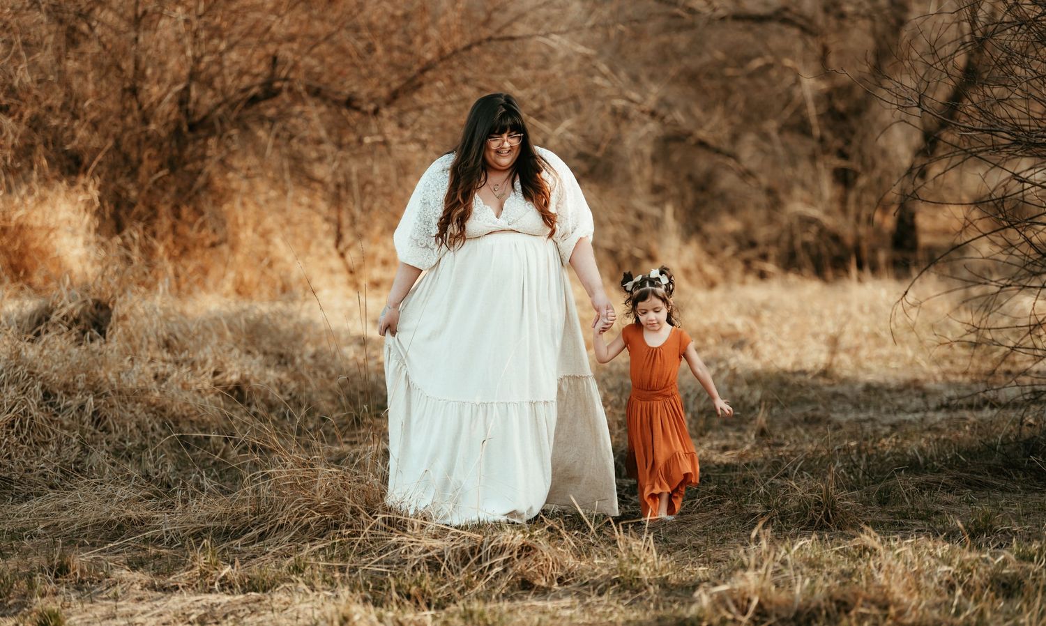 A white-dressed figure and small child in orange walk together in a rustic autumn field.