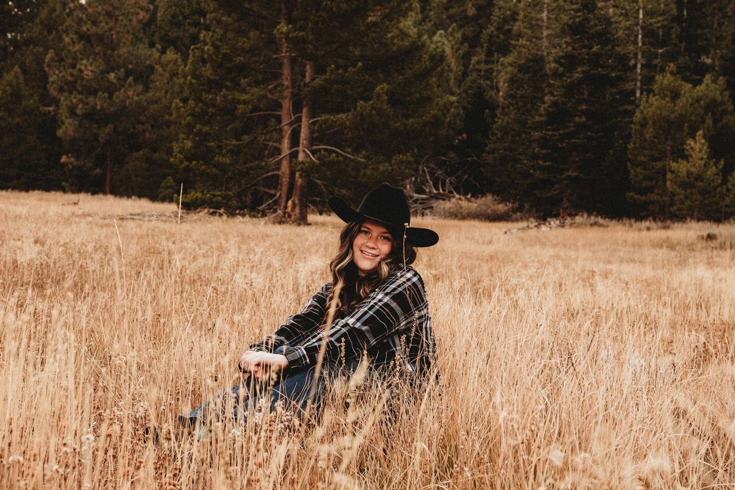 A casual autumn portrait in tall grass with pine trees in the background.
