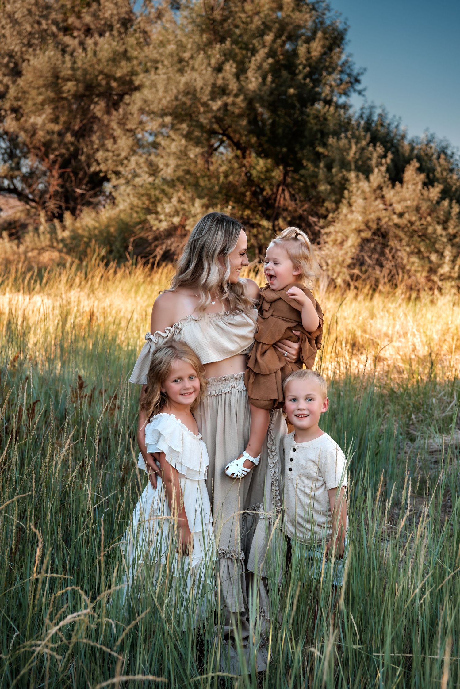 Family portrait with children in coordinating neutral outfits standing in meadow grass.