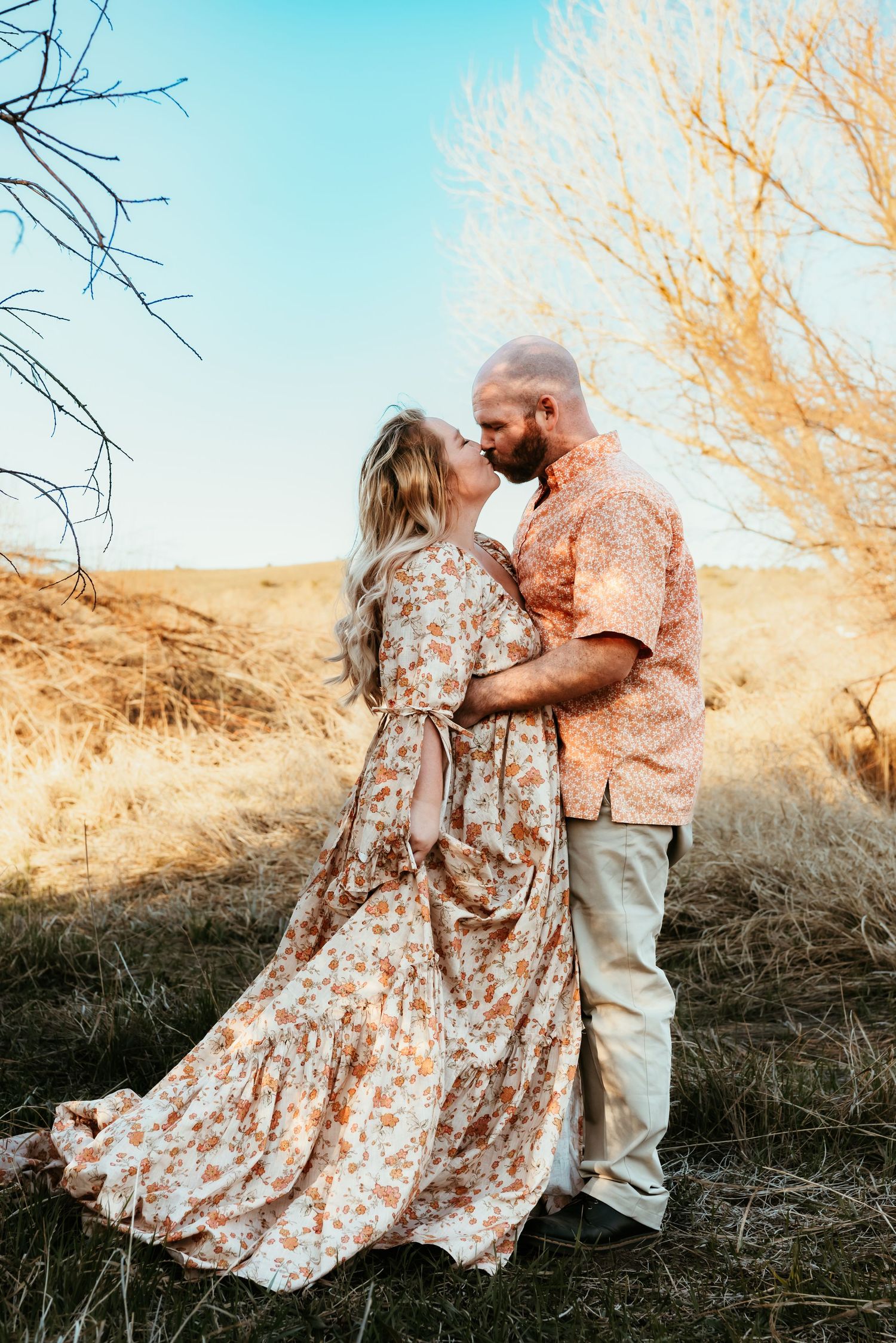 Romantic couple embraces in flowing dress against golden desert landscape.