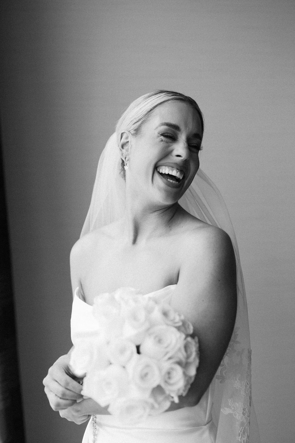 Black and white series of a joyful bride laughing and posing with a white rose bouquet.