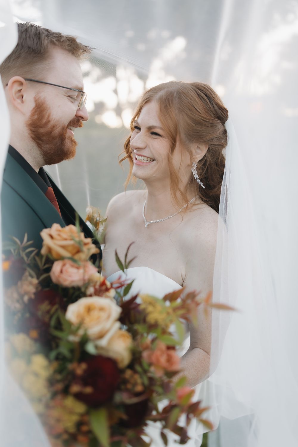 Romantic wedding couple shares intimate moments behind sheer white curtains with autumn-toned floral bouquet.