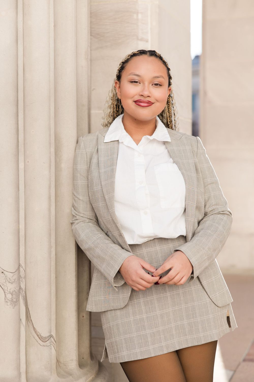 Business professional poses against cream colored columns in a gray blazer and white top.