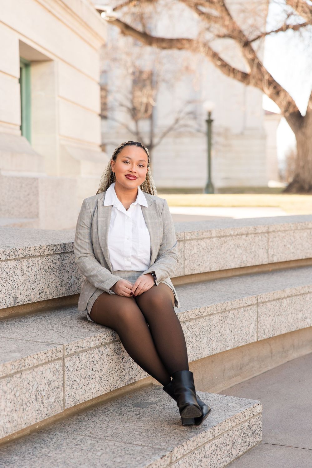 Professional in a gray blazer and white blouse sitting on concrete steps in an urban setting.