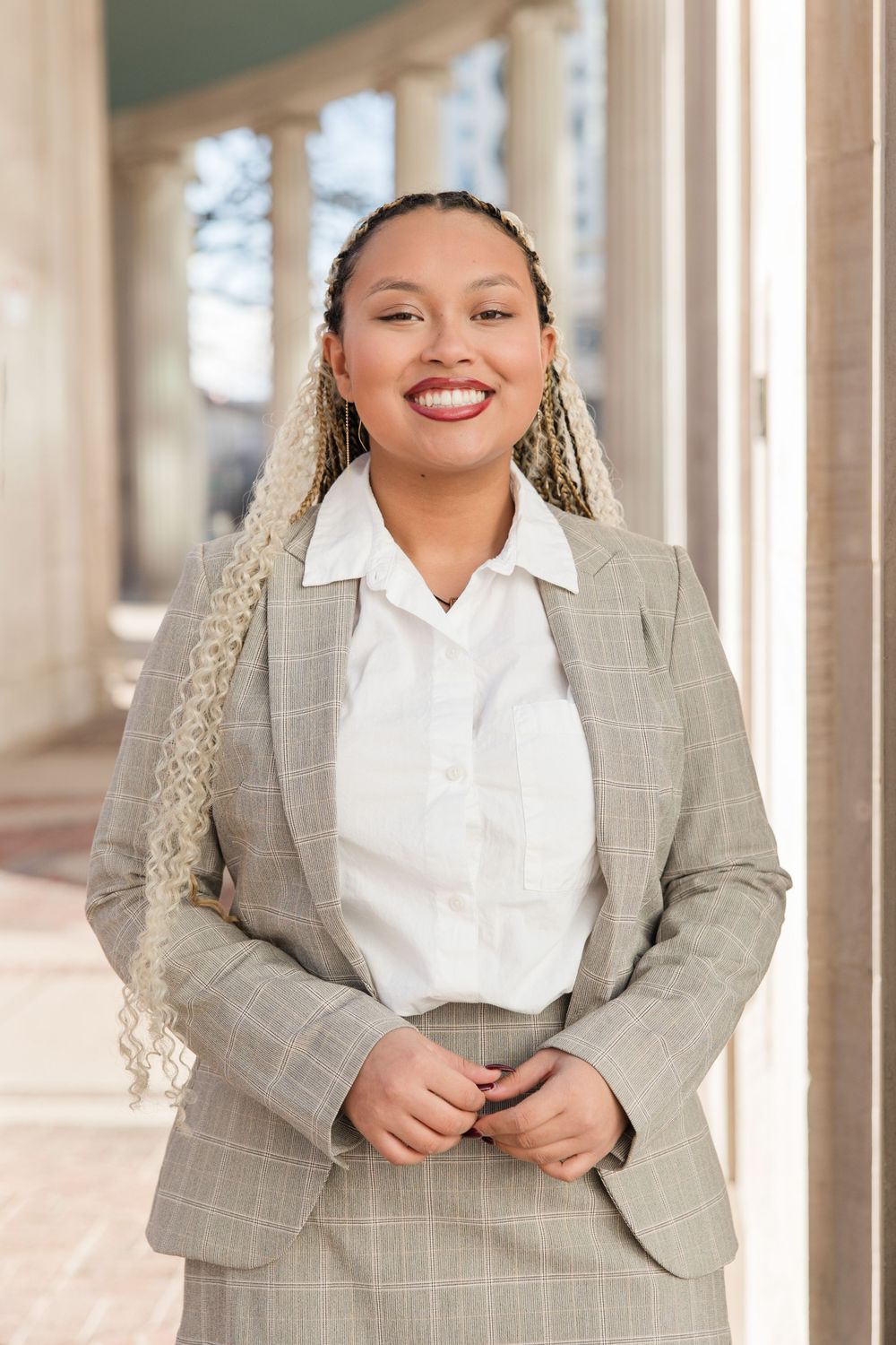 Professional portrait of someone wearing a gray plaid blazer and white blouse in front of architectural columns.