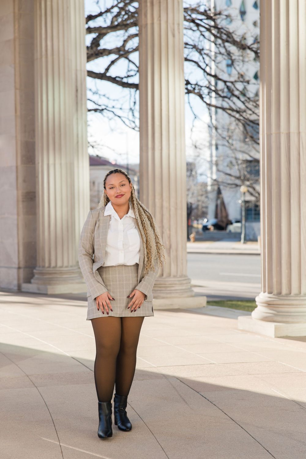 Fashion model posing between elegant stone columns in a grey plaid suit and black boots.