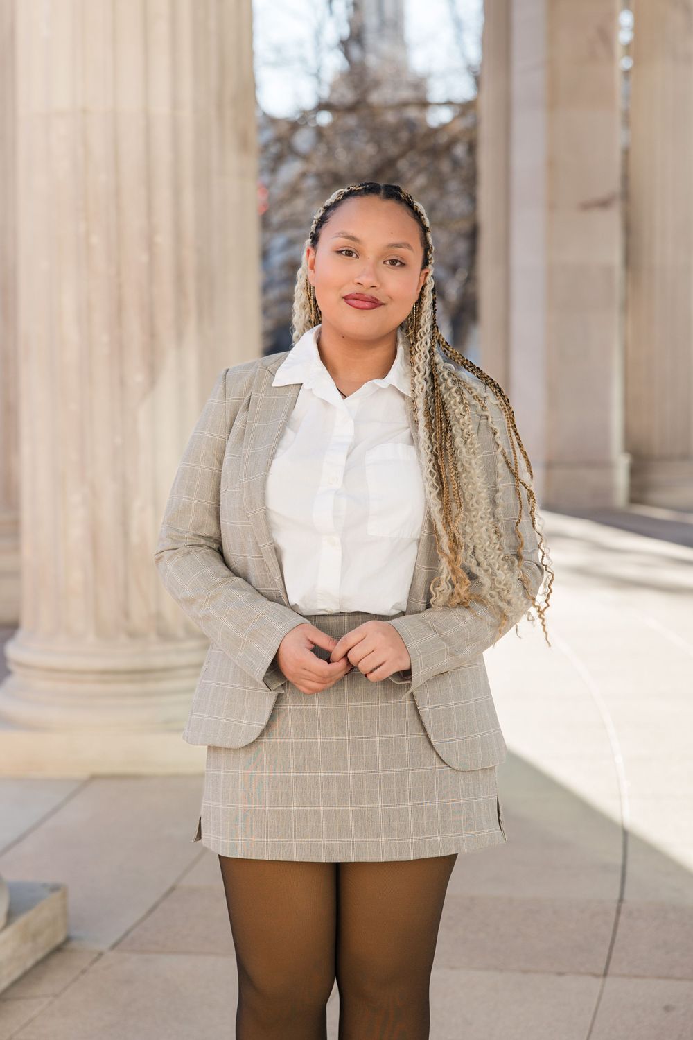 Professional portrait of someone in a gray blazer and white blouse posing against classical columns.