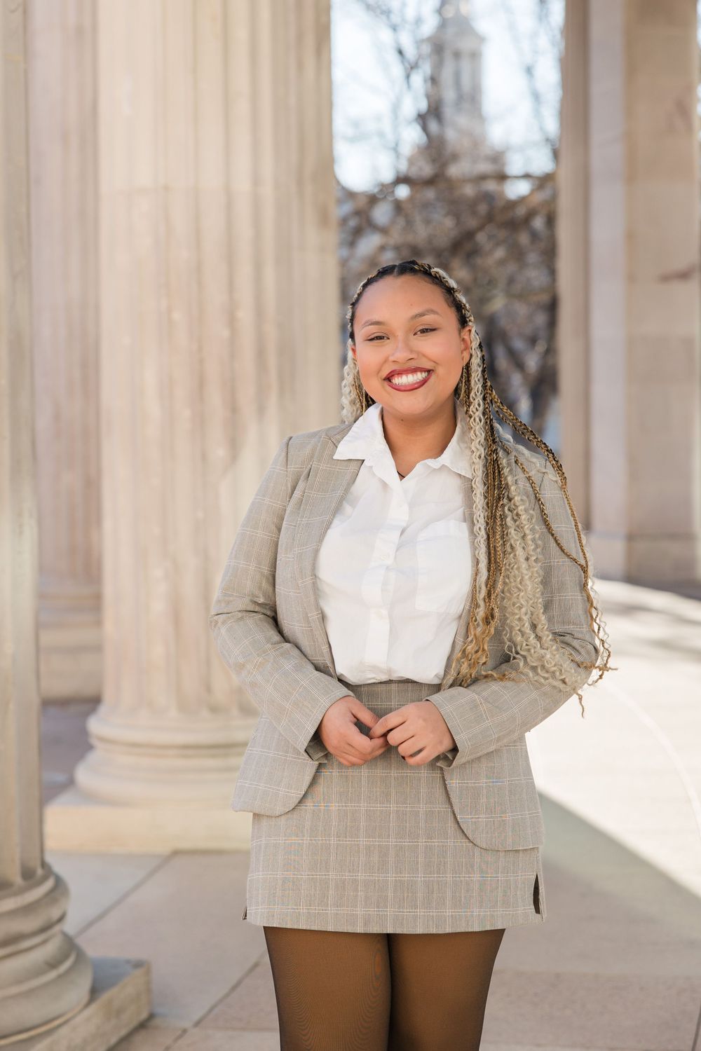 Professional fashion portrait in front of classical columns featuring a plaid blazer and white blouse outfit.
