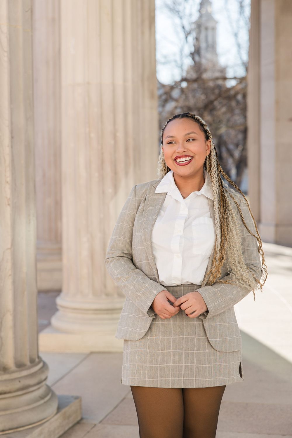 Professional fashion photo series showing a stylish winter outfit with plaid blazer and white blouse against stone columns.
