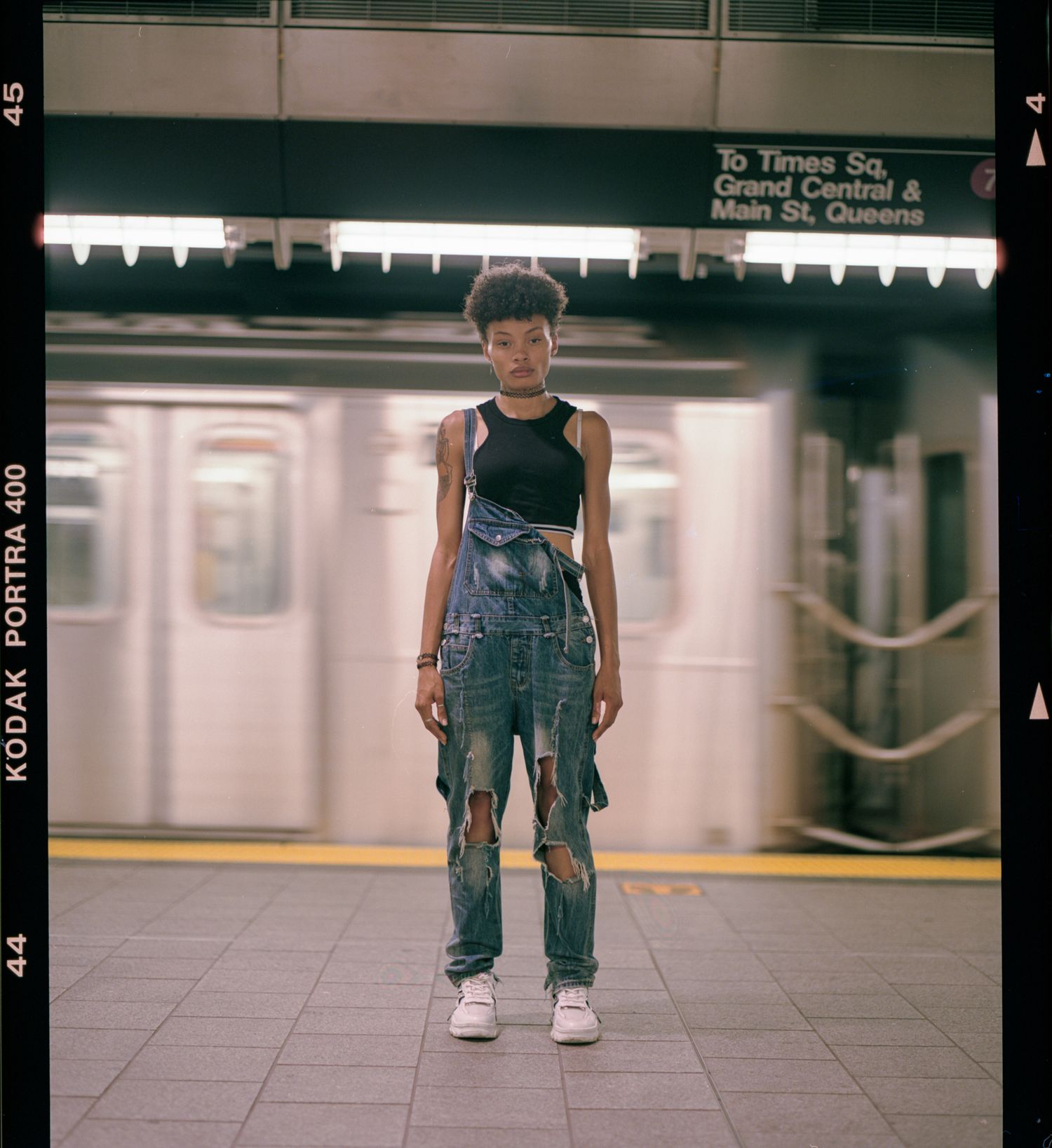 Person in denim overalls and white sneakers standing on a subway platform in a repeating panoramic view.