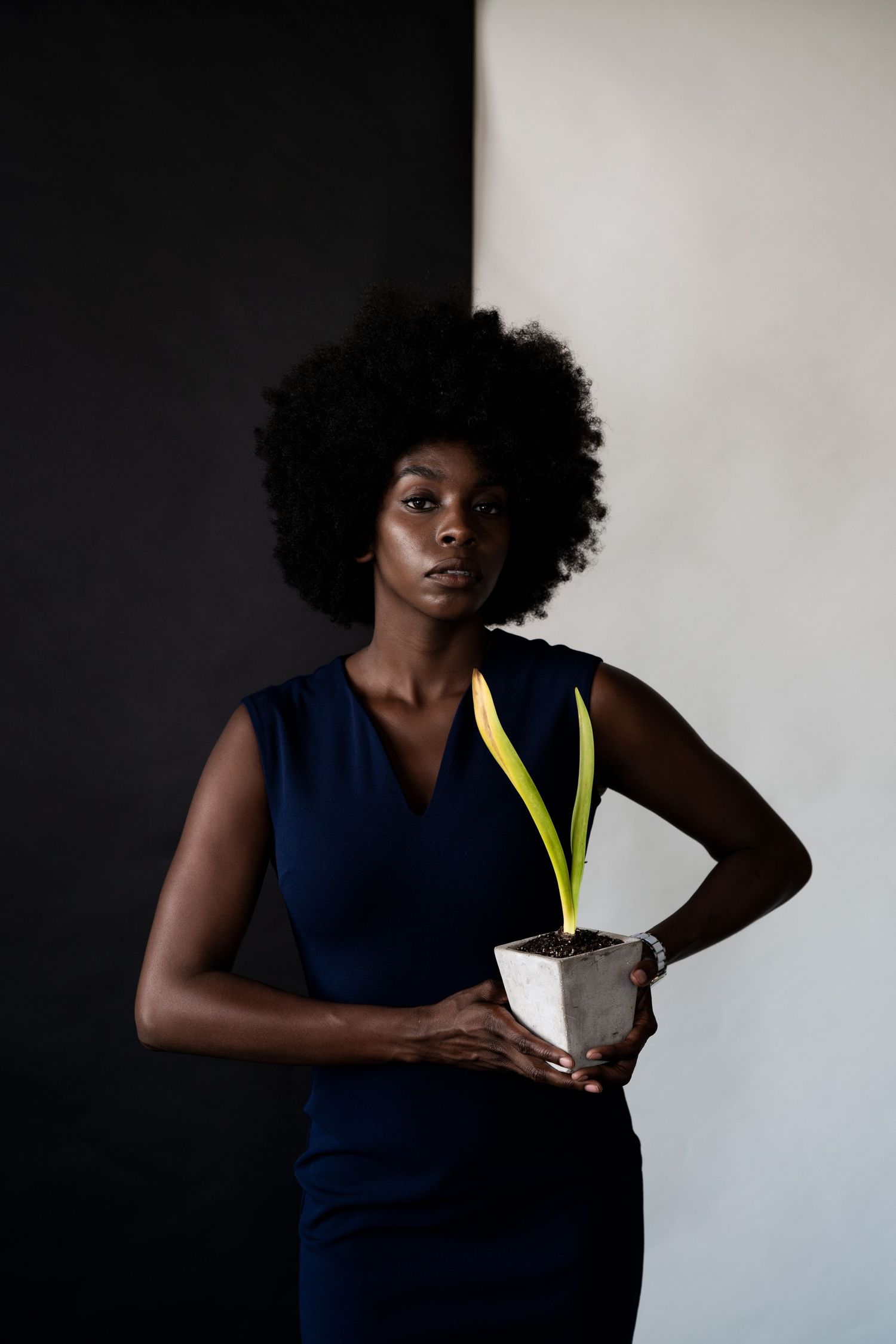 A person in a navy sleeveless dress holds a white cocktail with yellow garnish against a dark background.