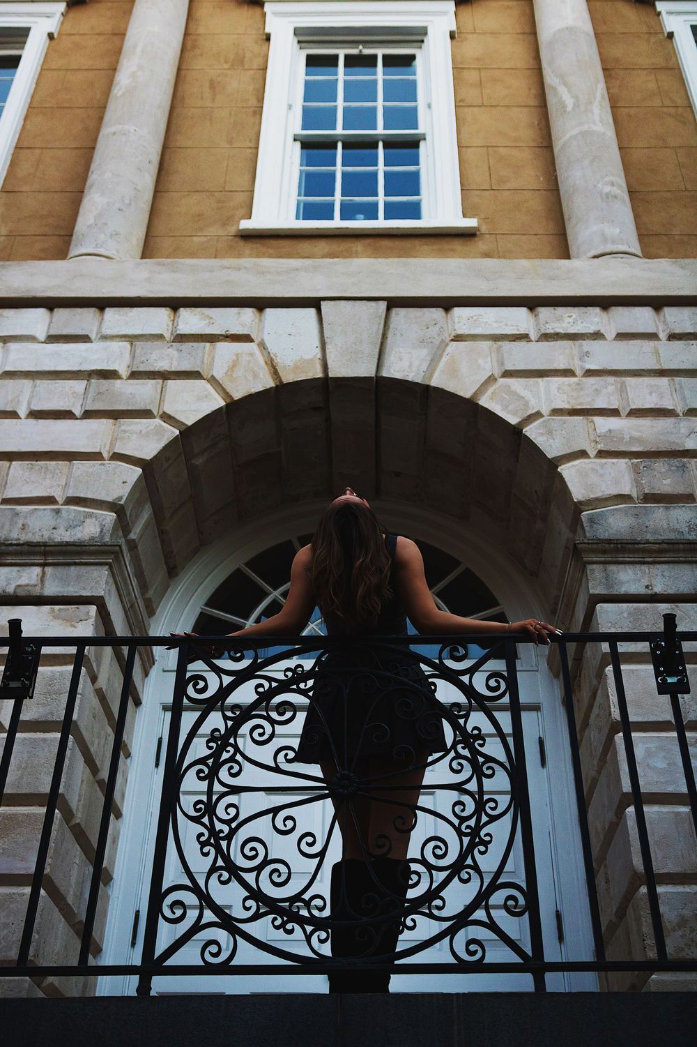 Silhouetted figure holding an umbrella stands beneath ornate arched columns of a historic stone building.
