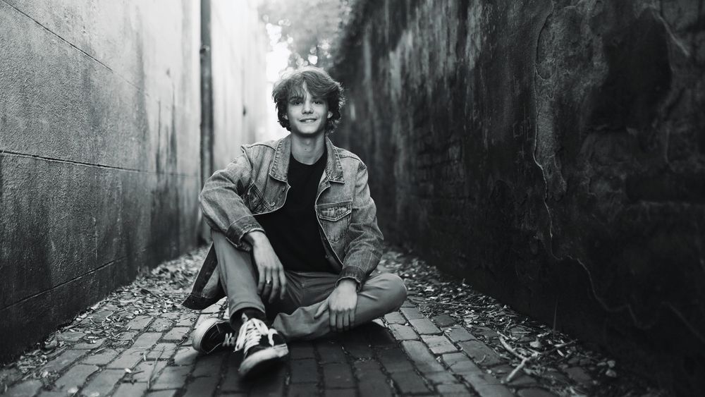 A black and white photo series shows a person sitting in various positions along a narrow urban alley.