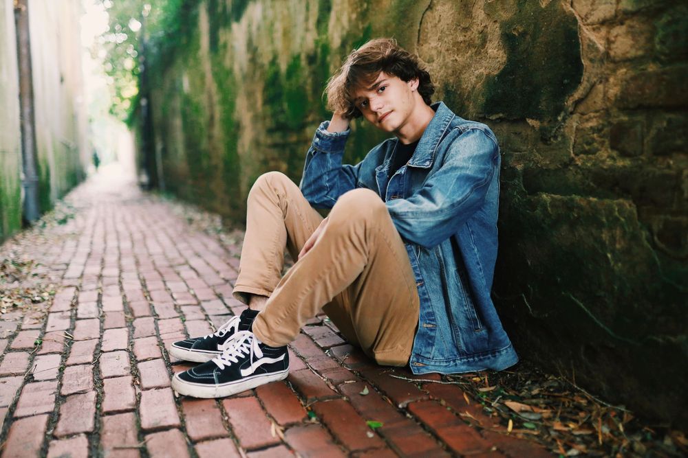 A person in casual attire sitting on brick steps against a stone wall in an outdoor garden setting.