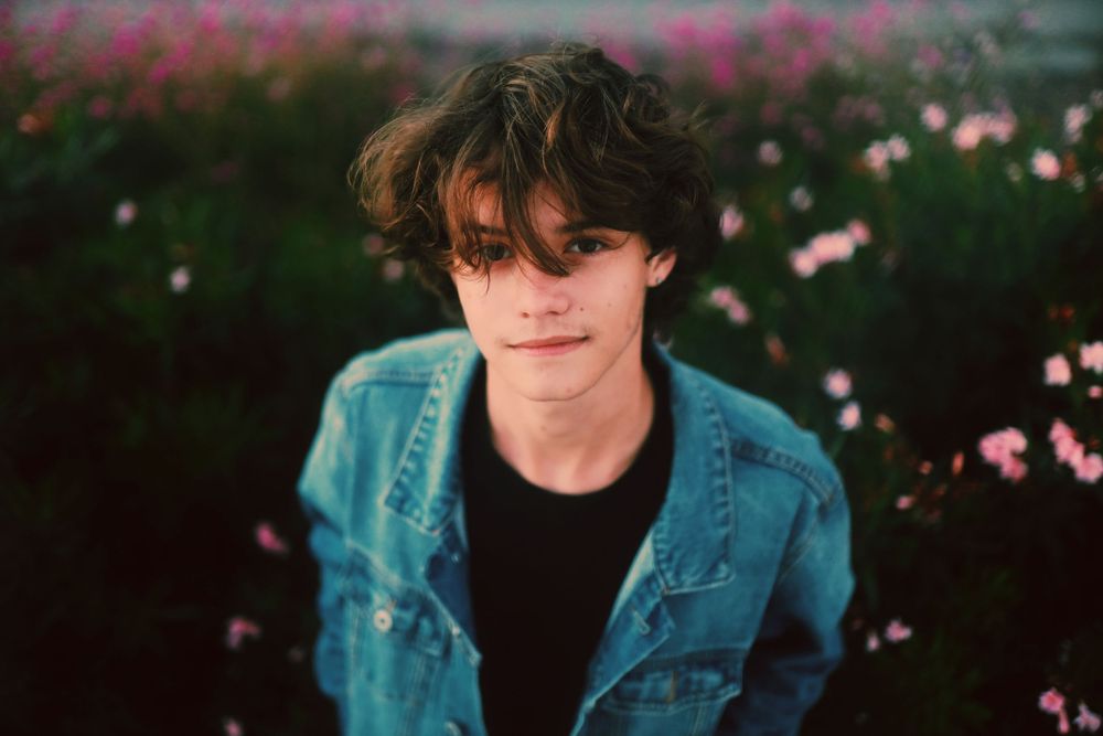 Person in denim jacket poses in garden with pink cosmos flowers creating a dreamy outdoor aesthetic.