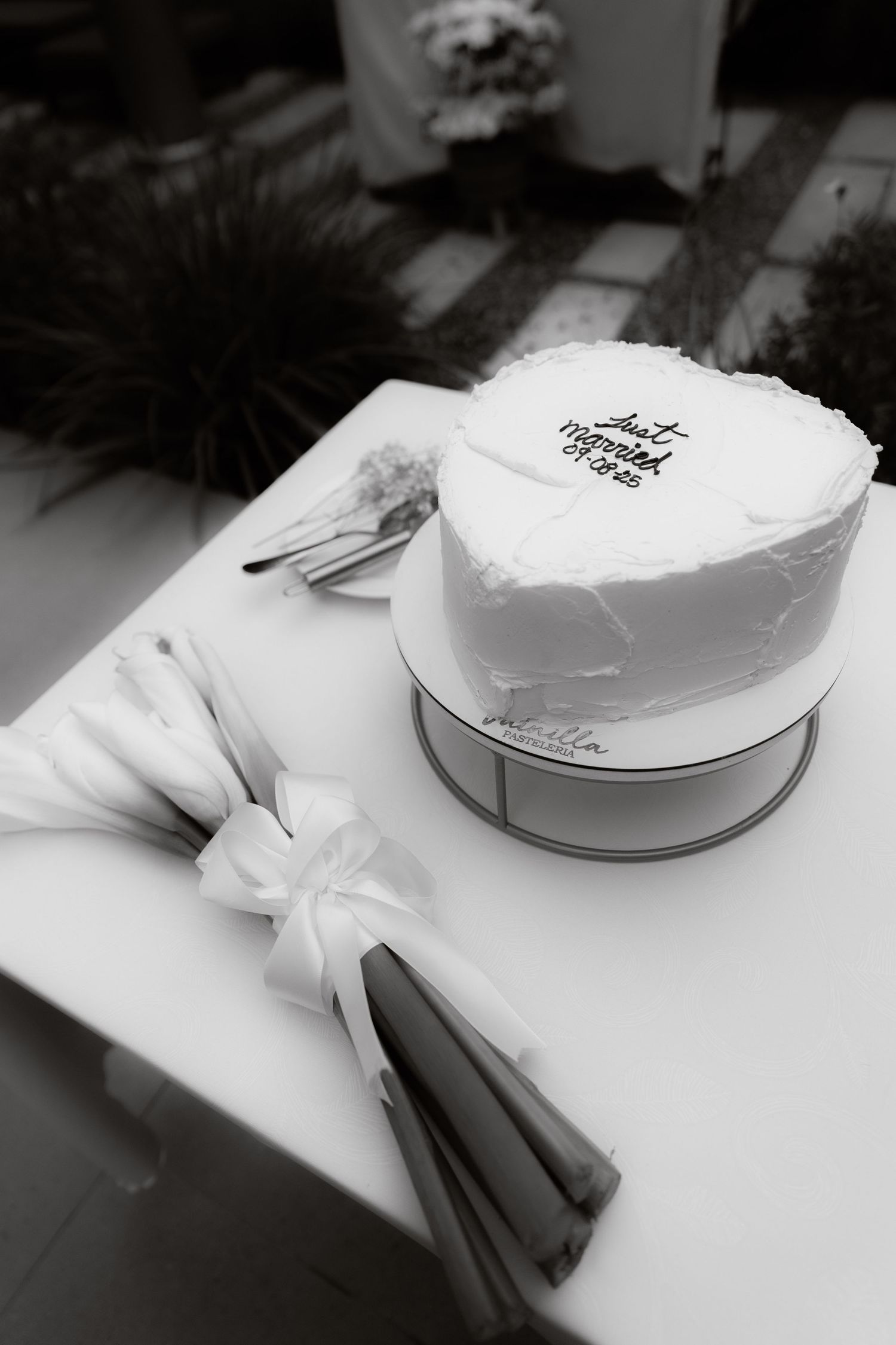 Black and white photo of a heart-shaped wedding cake with just married inscription on a white table.