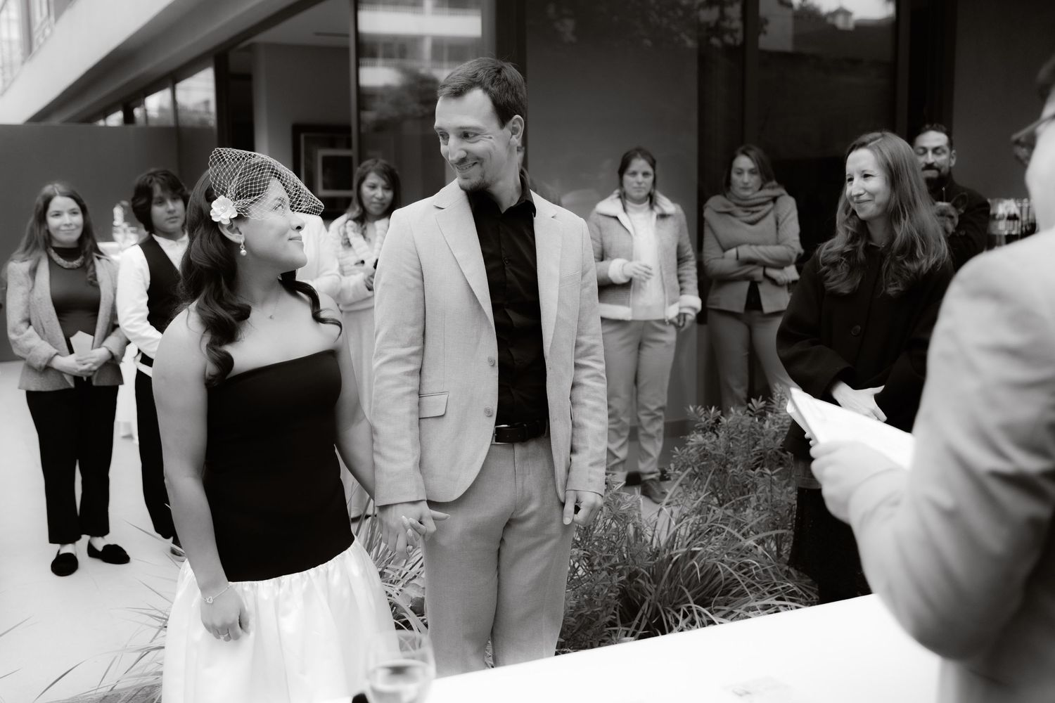 Black and white photo of couple at outdoor wedding ceremony with guests.