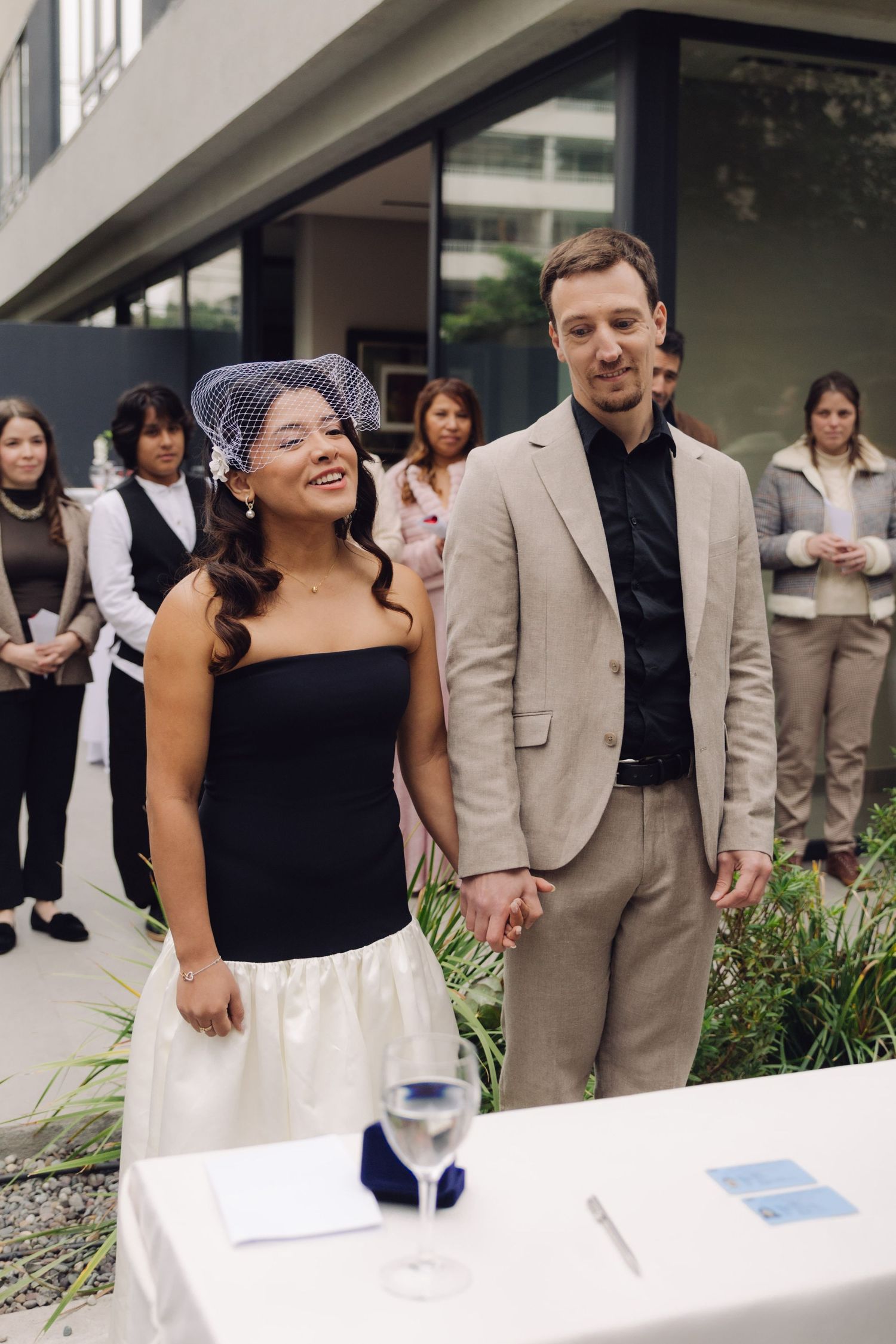 Bride in black top and white skirt holds groom's hand at wedding ceremony.