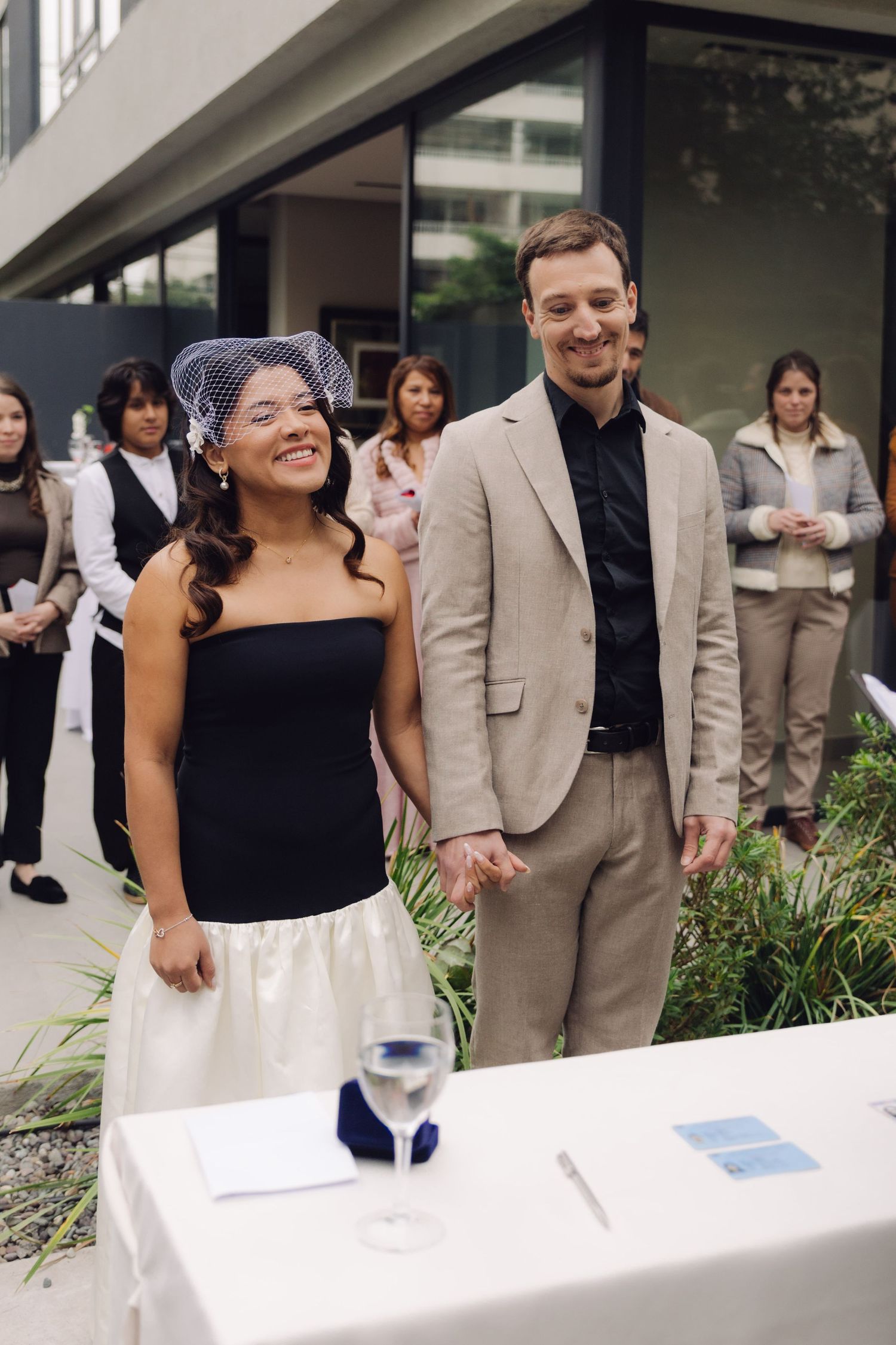 Smiling bride and groom hold hands at outdoor wedding ceremony table.