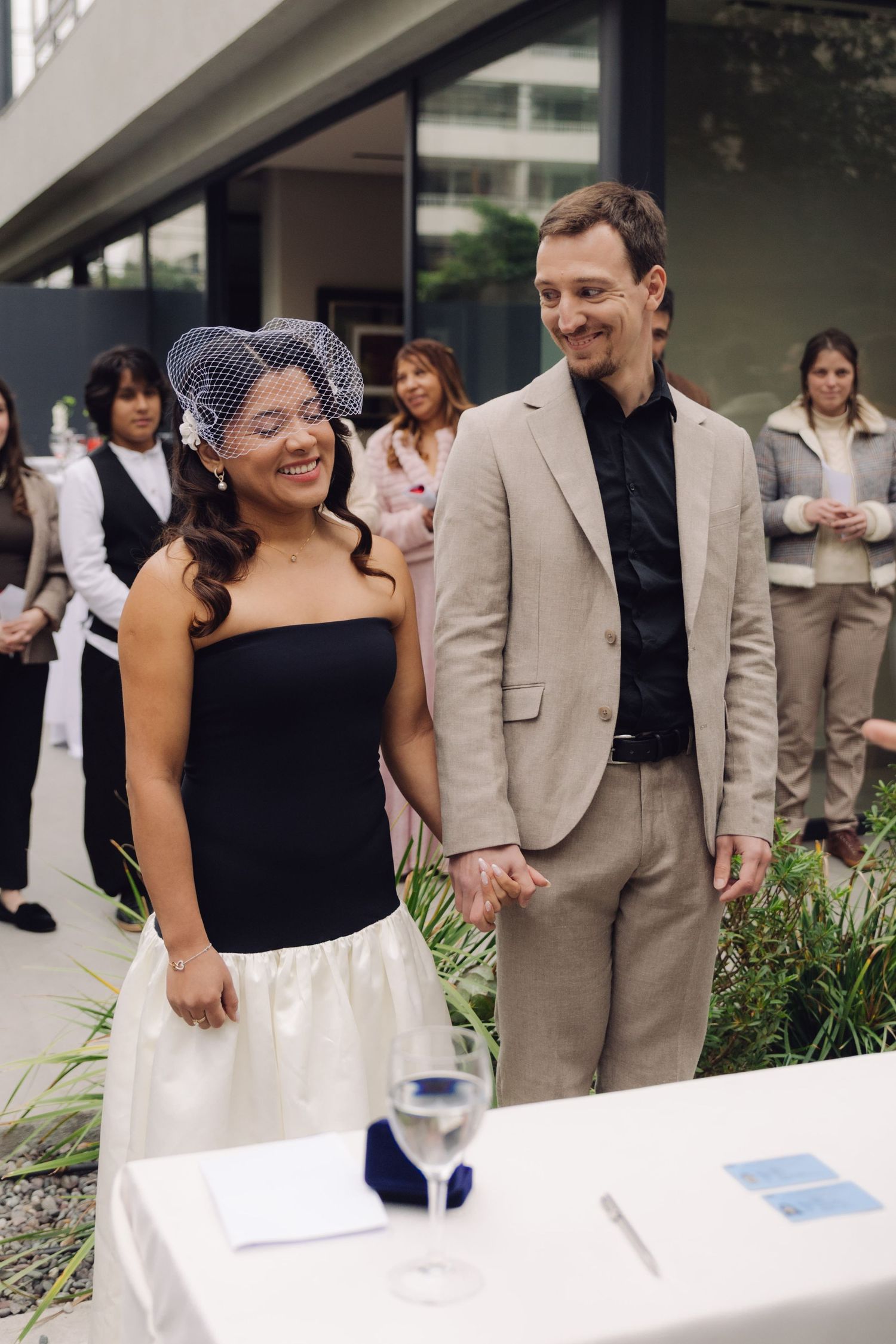 Happy couple holds hands during outdoor wedding ceremony with guests behind them.