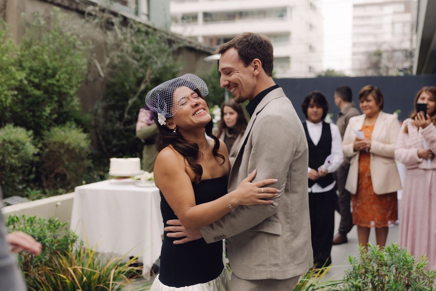 Bride and groom laughing joyfully together at outdoor wedding reception surrounded by guests.