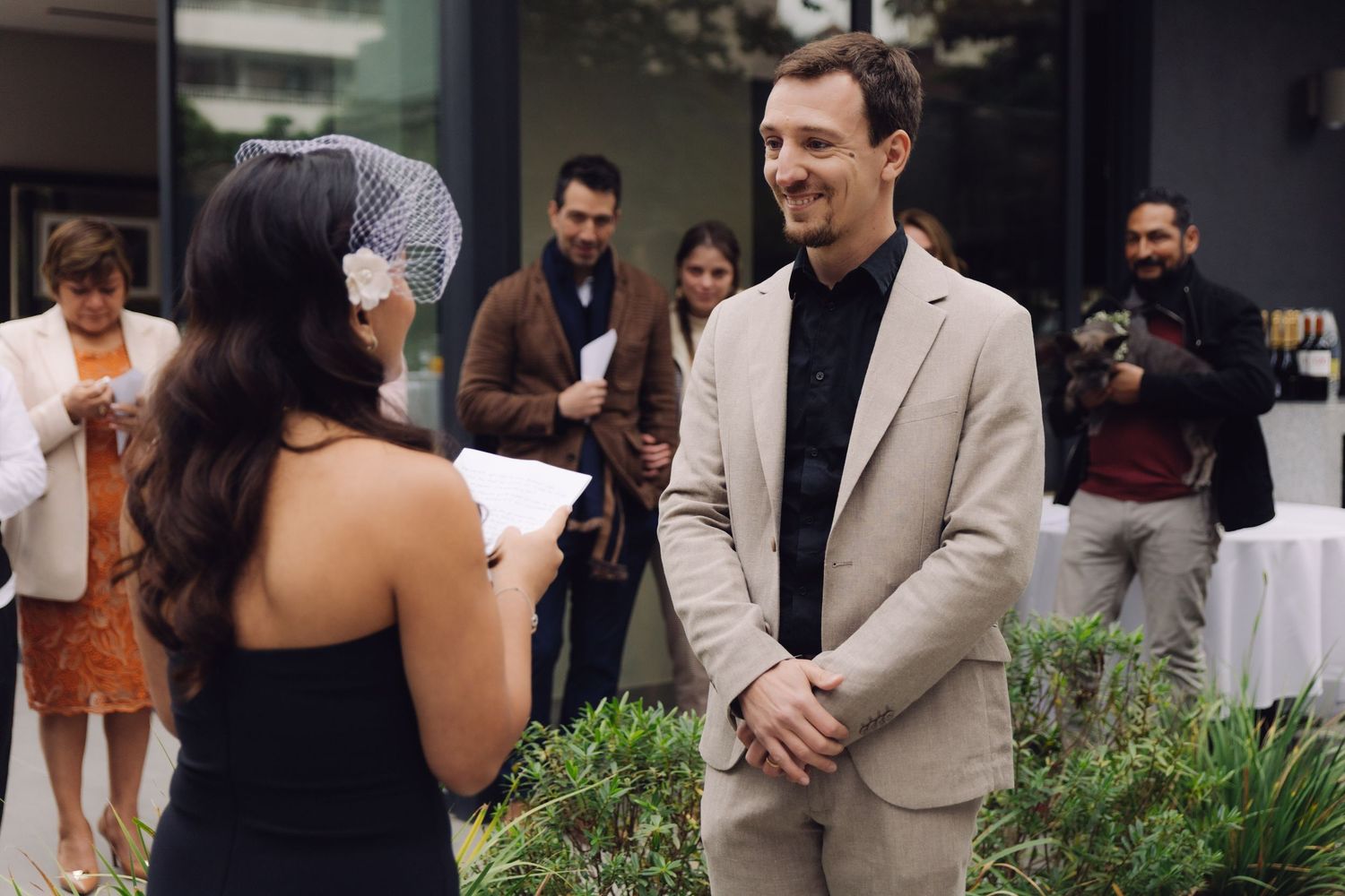 Bride reading handwritten wedding vows to smiling groom at outdoor ceremony.