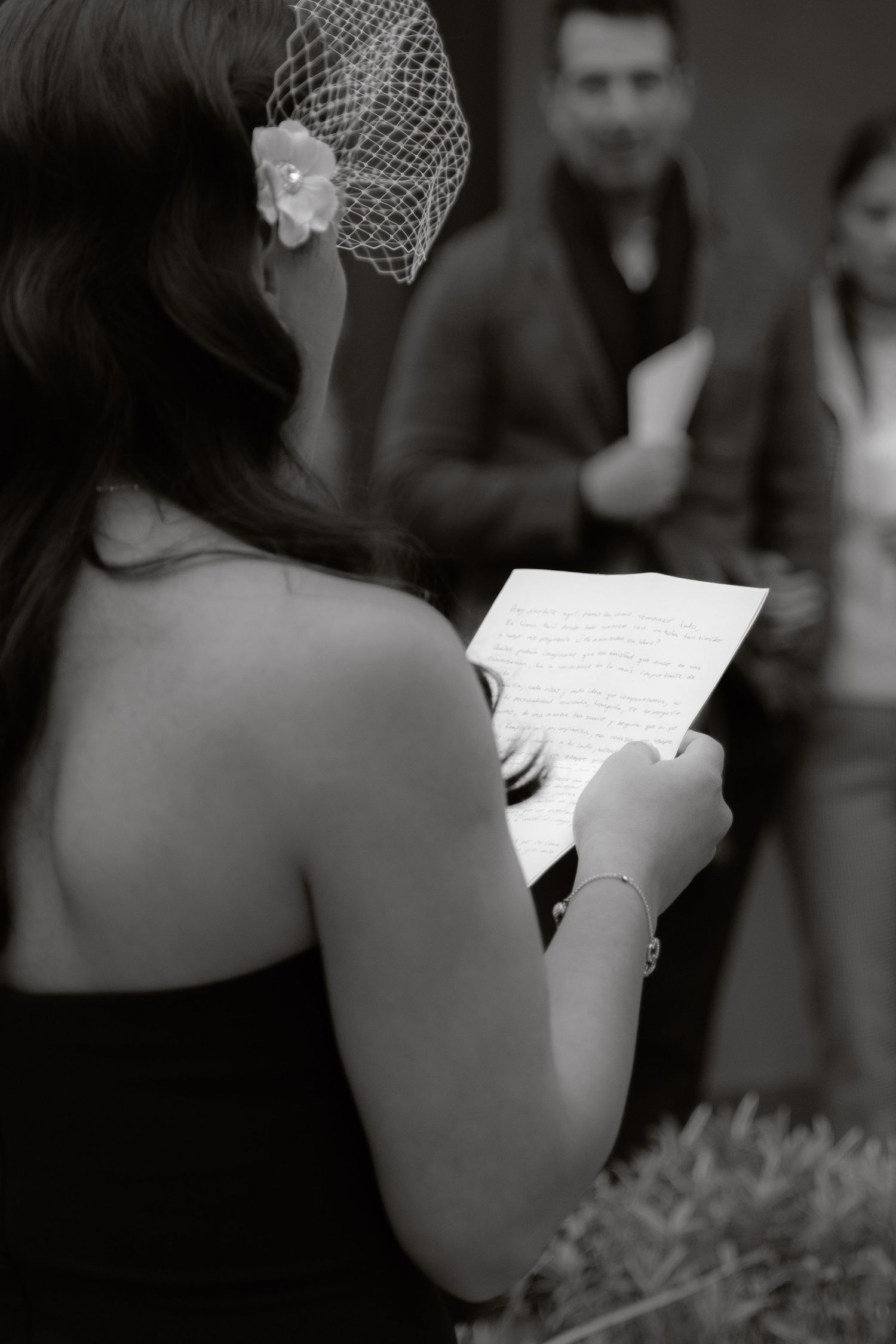Black and white photo of bride reading handwritten vows at wedding ceremony.
