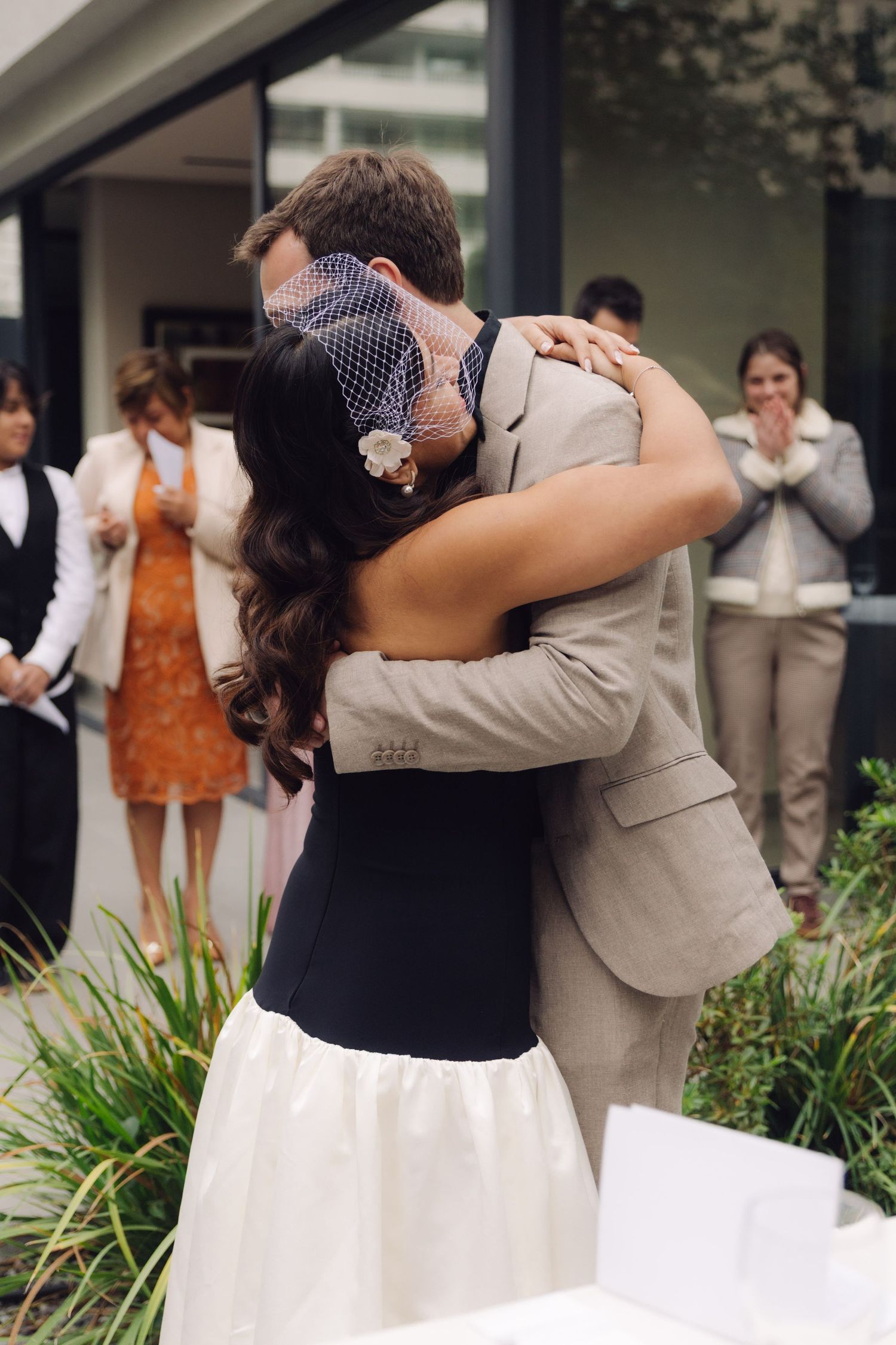 Bride and groom share a romantic first kiss embrace at outdoor wedding ceremony while guests watch.