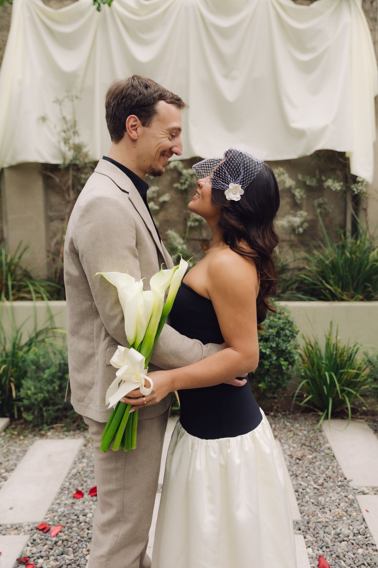 Smiling bride and groom holding white calla lilies in garden wedding ceremony setting.