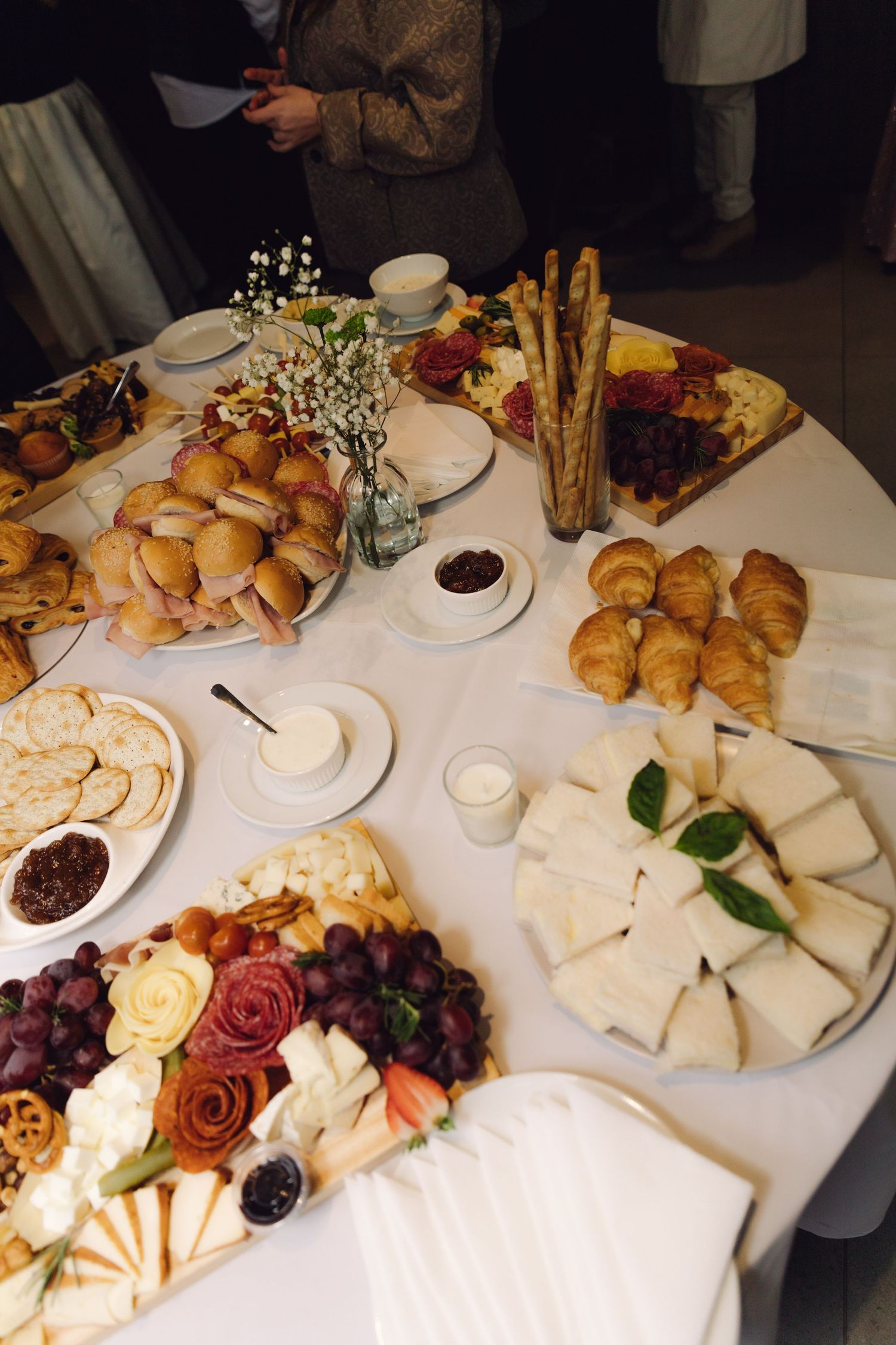 Elegant round wedding reception table with croissants, cheese board, charcuterie and fresh flowers.