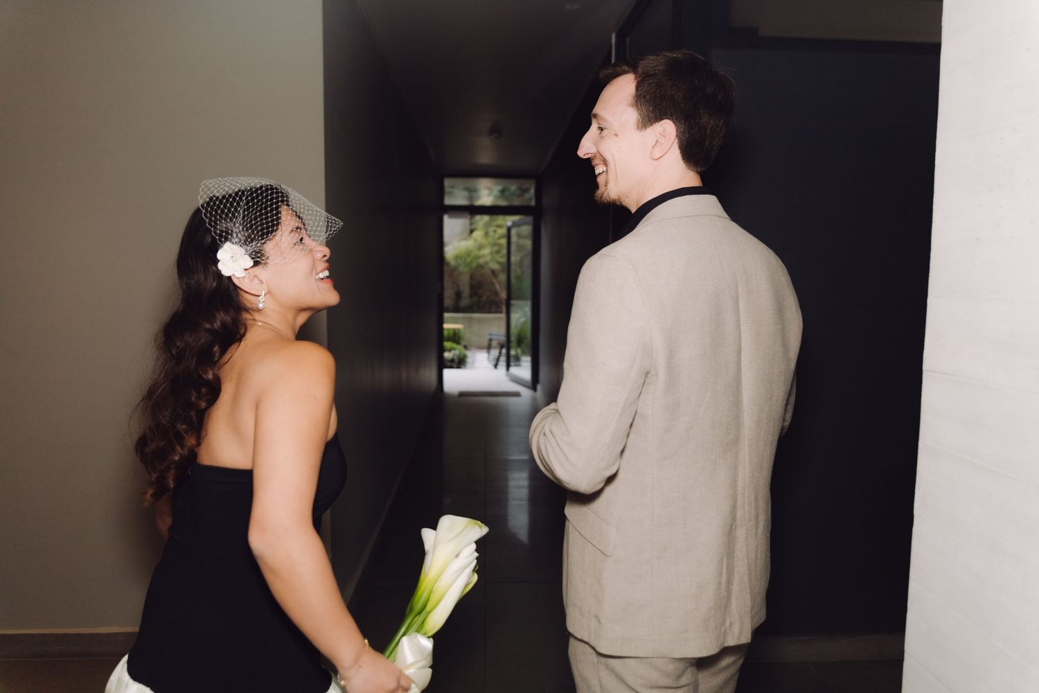 Smiling bride and groom share a joyful moment in a hallway during their wedding day.