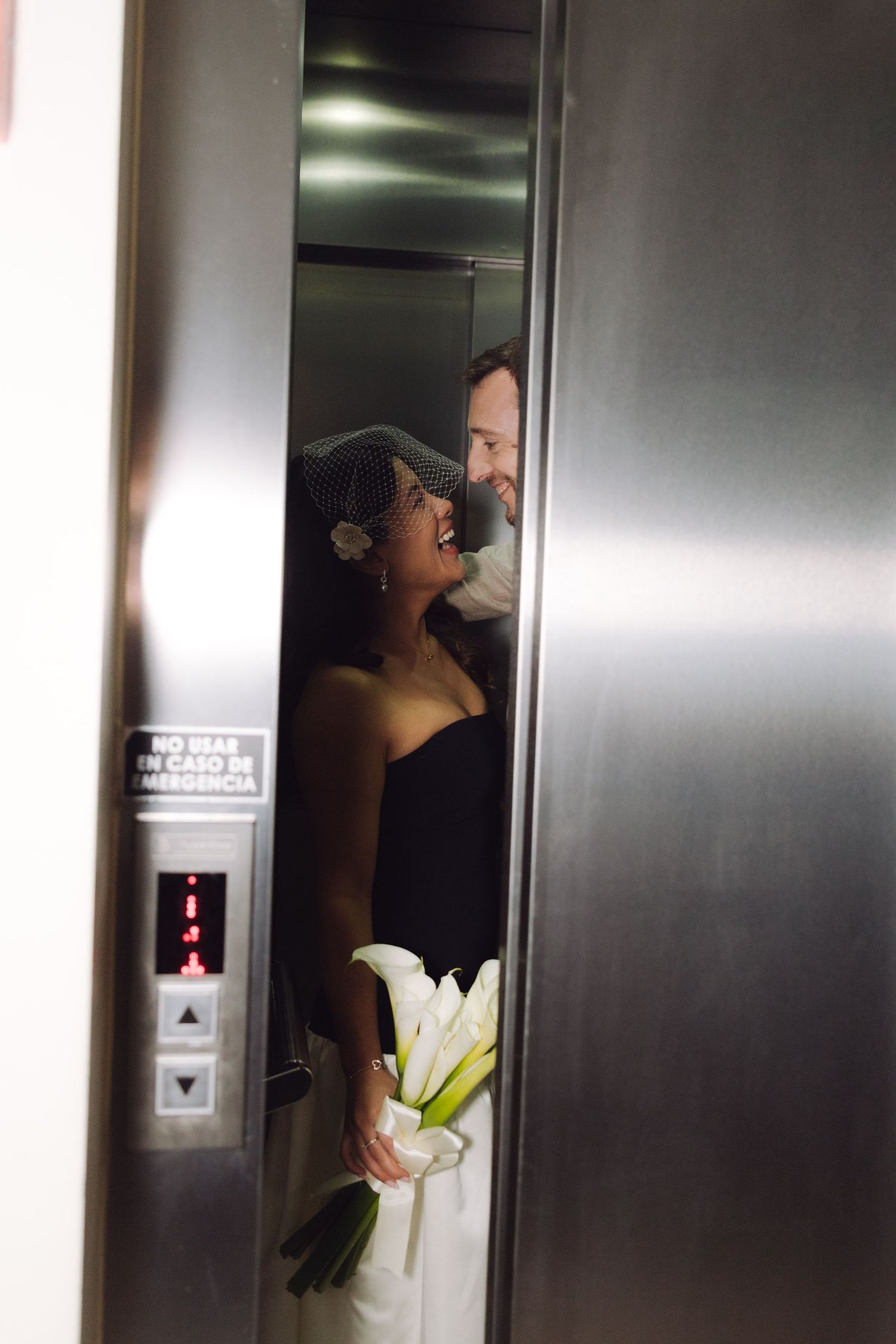 Bride and groom share a romantic laugh inside a silver elevator on their wedding day.