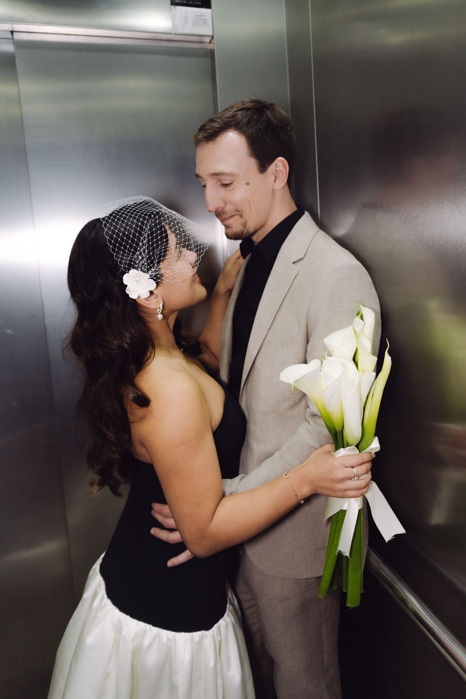 Bride and groom share a romantic moment in an elevator, bride holding white calla lily bouquet wearing birdcage veil.