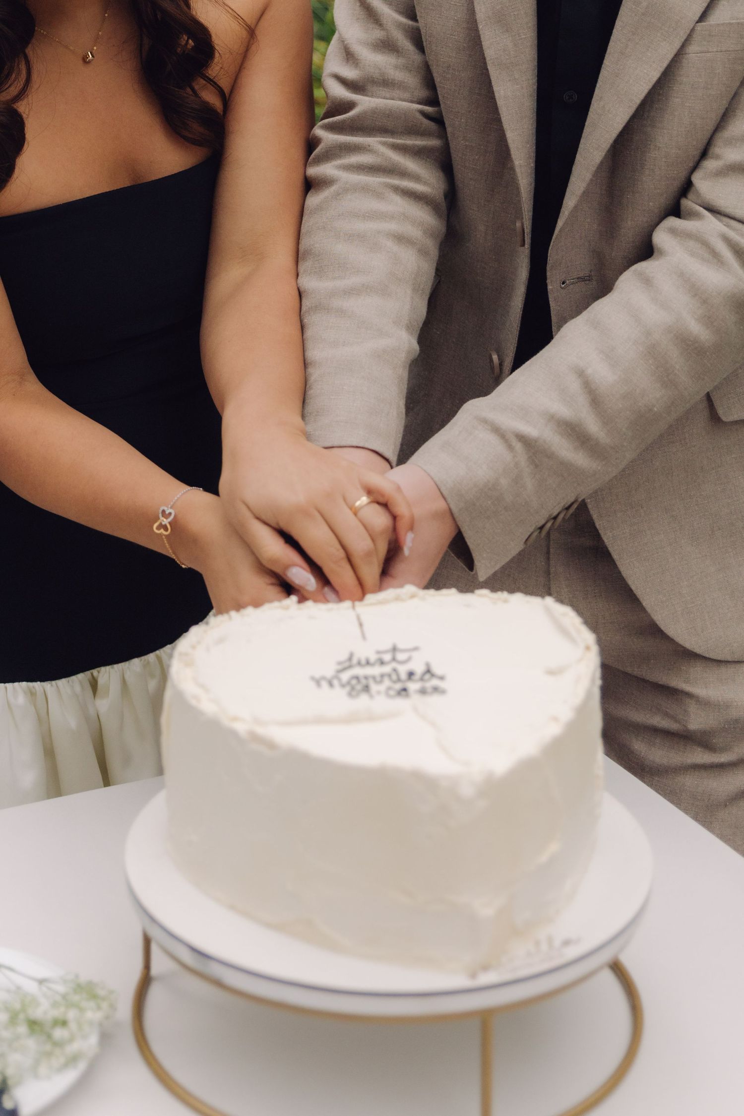 Close-up of bride and groom hands cutting heart-shaped white wedding cake inscribed with just married at reception.