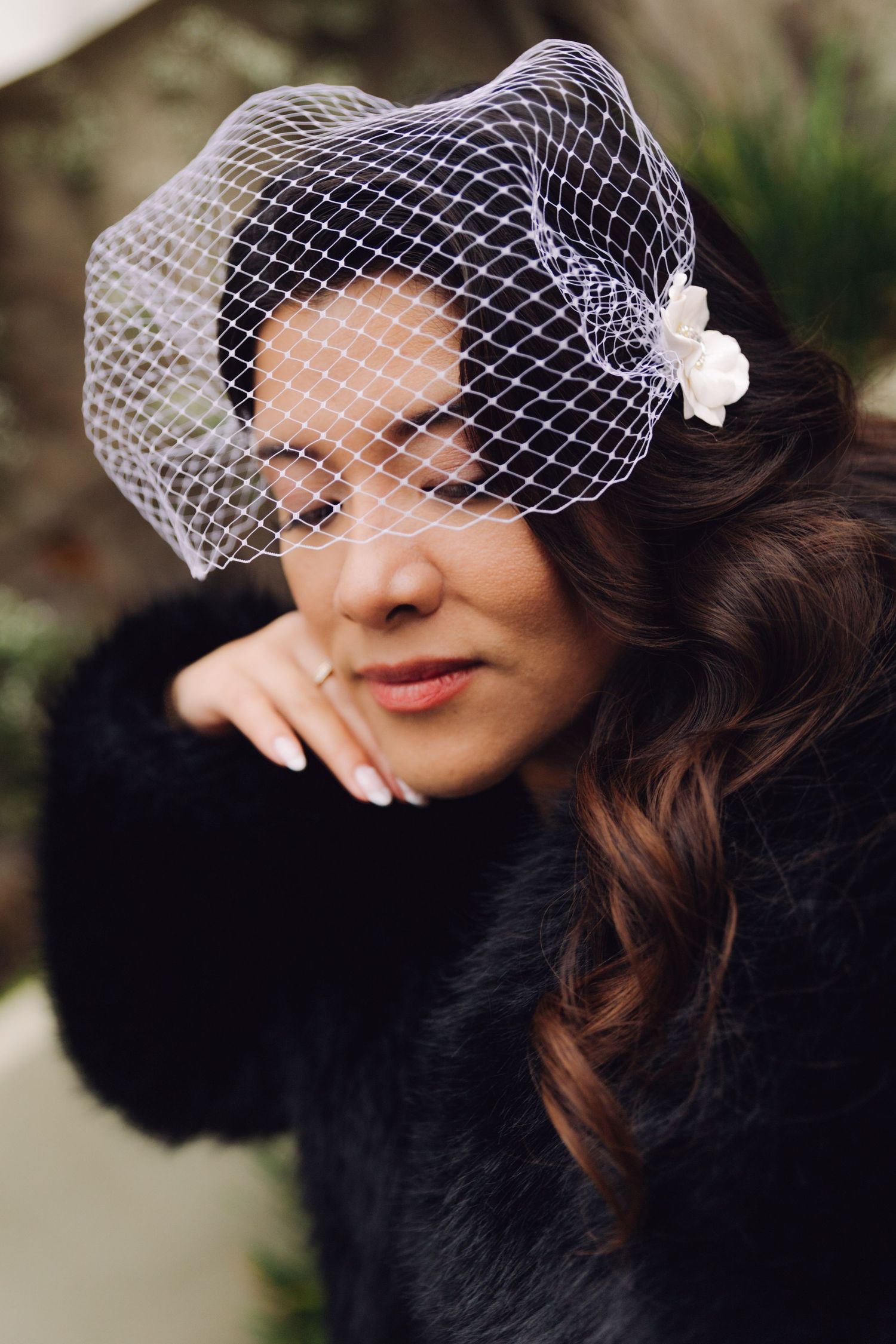 Close-up portrait of bride in black fur coat wearing white birdcage veil with flower.