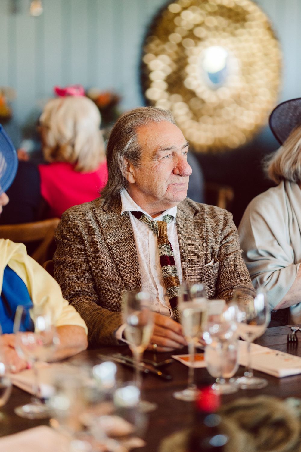 Elegantly dressed guest in tweed jacket and bowtie seated at formal dining table during celebration.