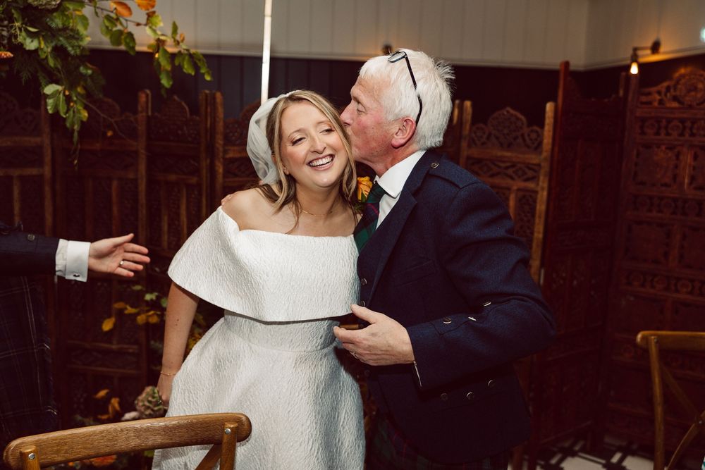 Wedding couple dancing and laughing together in an intimate venue with warm lighting and brick walls.