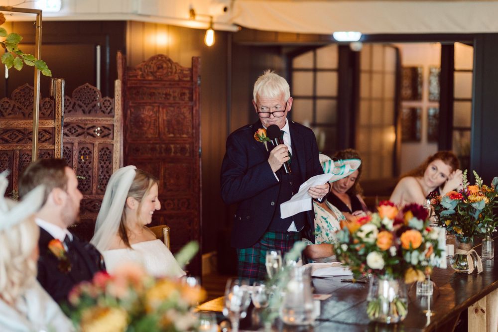 Wedding reception guests enjoy an intimate candlelit dinner with floral centerpieces in an elegant indoor venue.