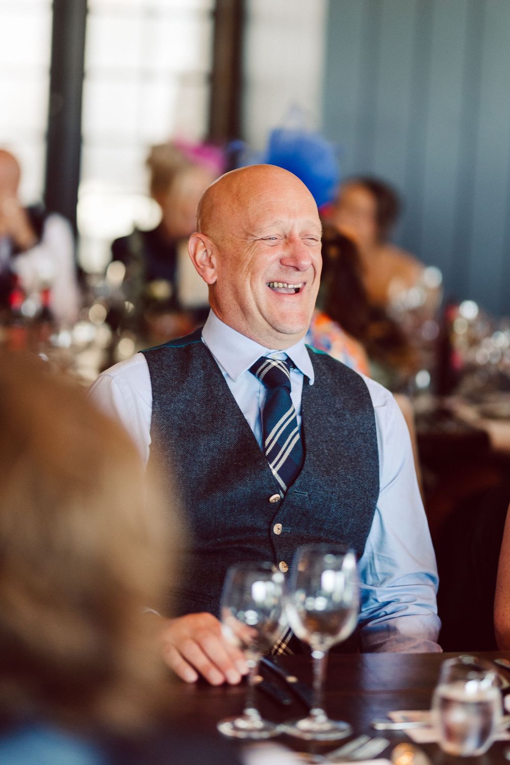 Joyful guest in waistcoat and tie laughing during formal dinner celebration.