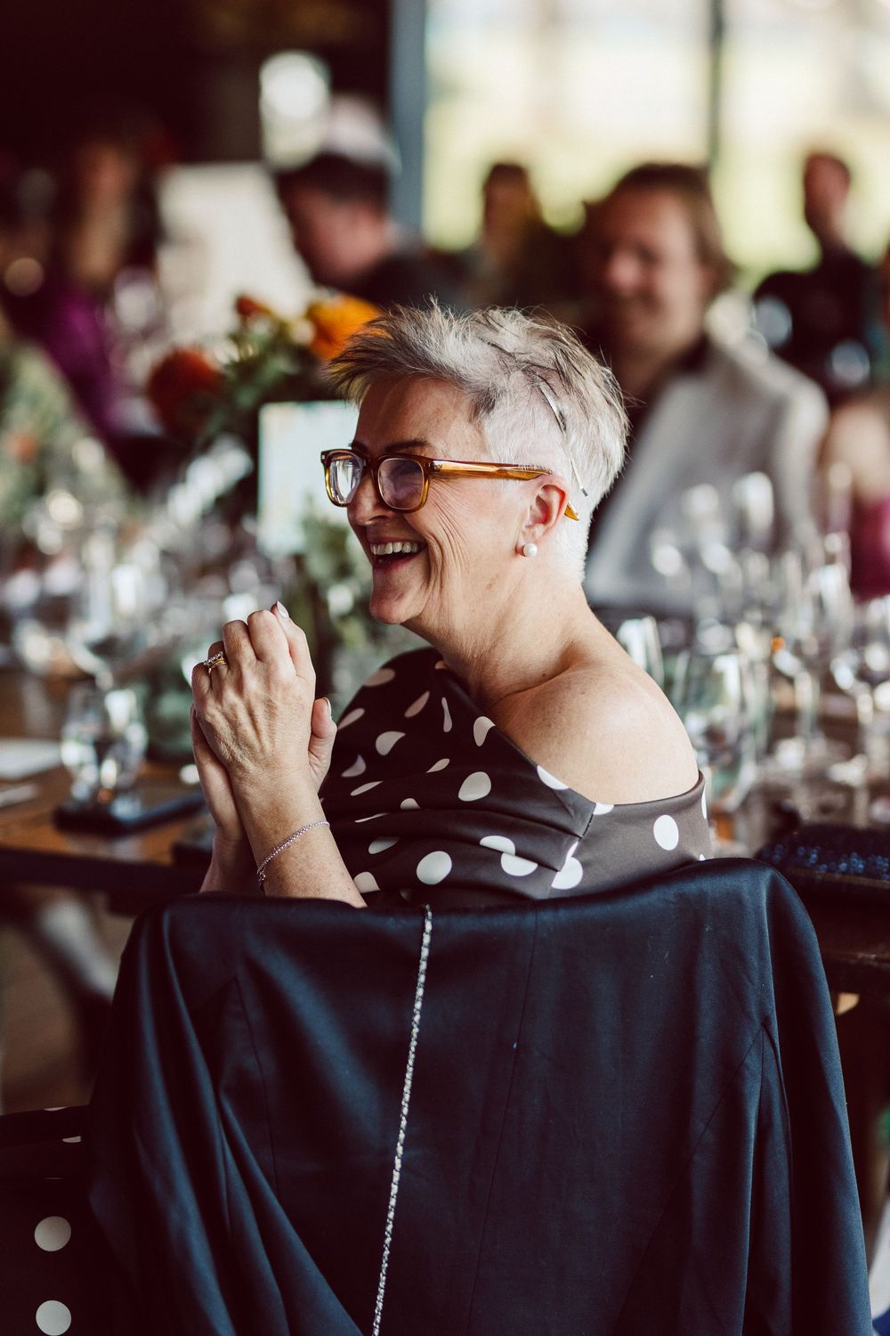 Guest in polka dot dress laughing heartily at formal dinner gathering.