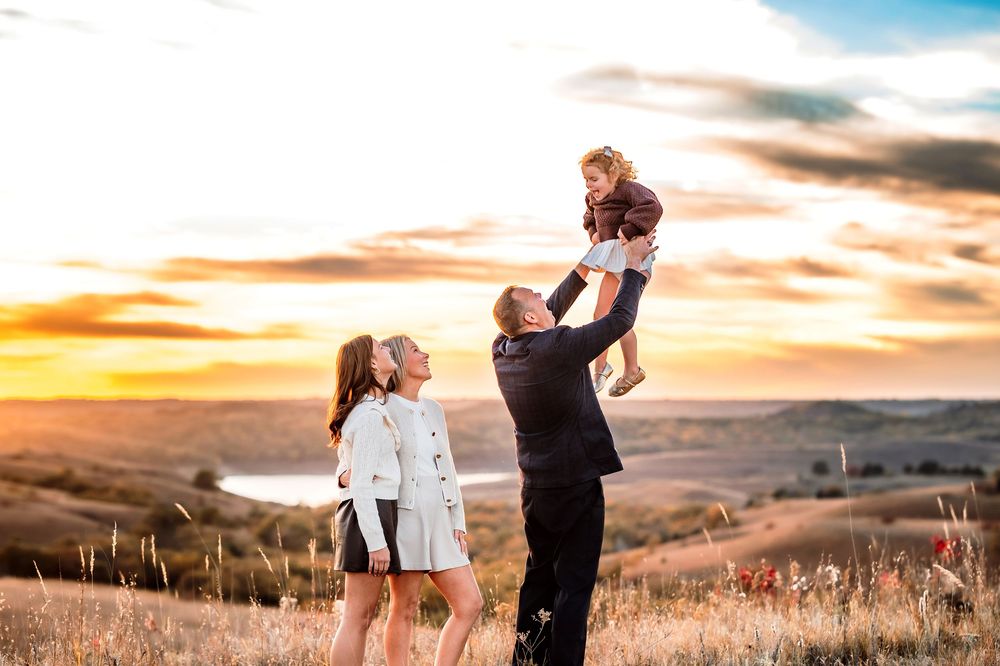 A couple embraces in silhouette against a dramatic sunset sky over rolling hills and tall grass.