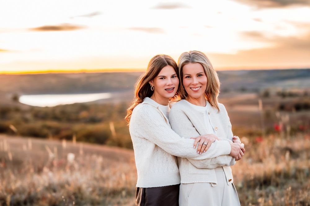 Two people in white sweaters embrace while laughing together during golden hour in a scenic outdoor setting.