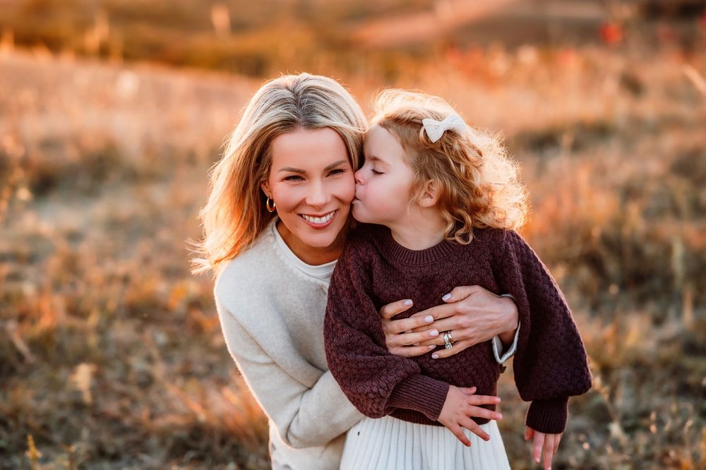 Candid moment between parent and child laughing together in golden autumn field at sunset.
