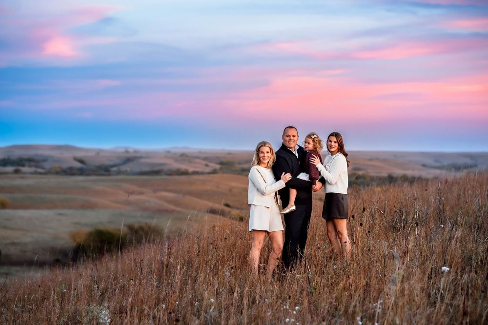 A group stands together in a golden field at sunset against rolling hills in the background.