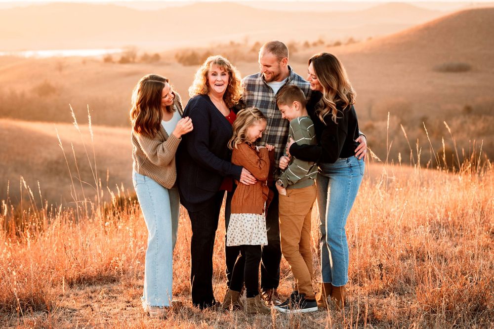 A family laughs together while sitting in a golden field at sunset during a photo session.